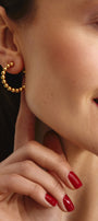 Close-up of a woman wearing gold hoop earrings and a bracelet, with red nail polish.