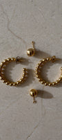 Gold hoop earrings with beads on a beige surface