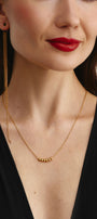 Woman wearing a gold necklace with small beads and long mono earring