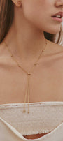 Woman wearing a gold necklace with small beads against a neutral background