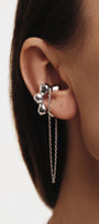 Close-up of a person wearing a silver flower-shaped earring with a chain 