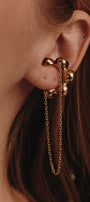 Gold mono earring with chain detail worn by a person