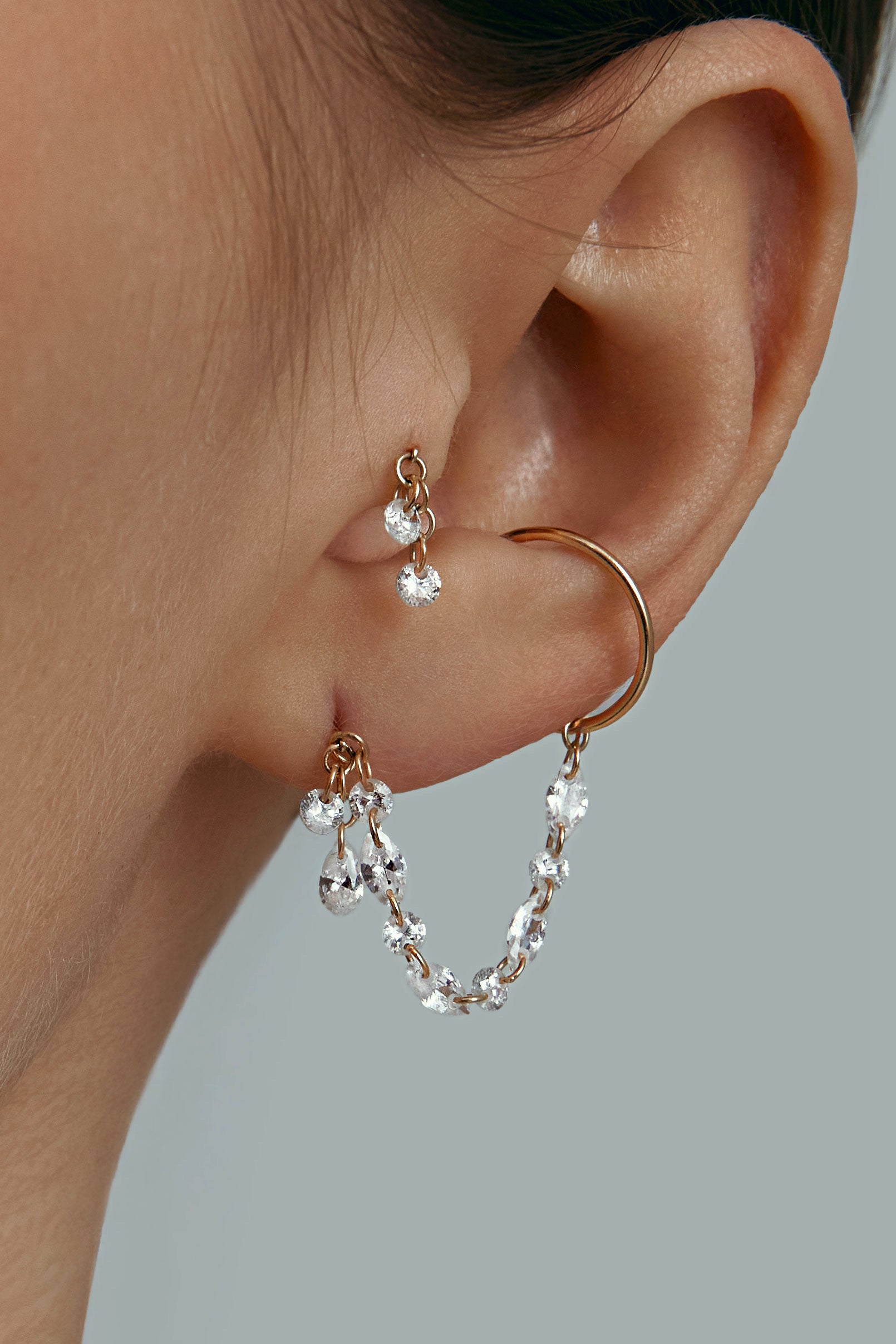 Close-up of an ear wearing gold cuff and tiny earrings with gems
