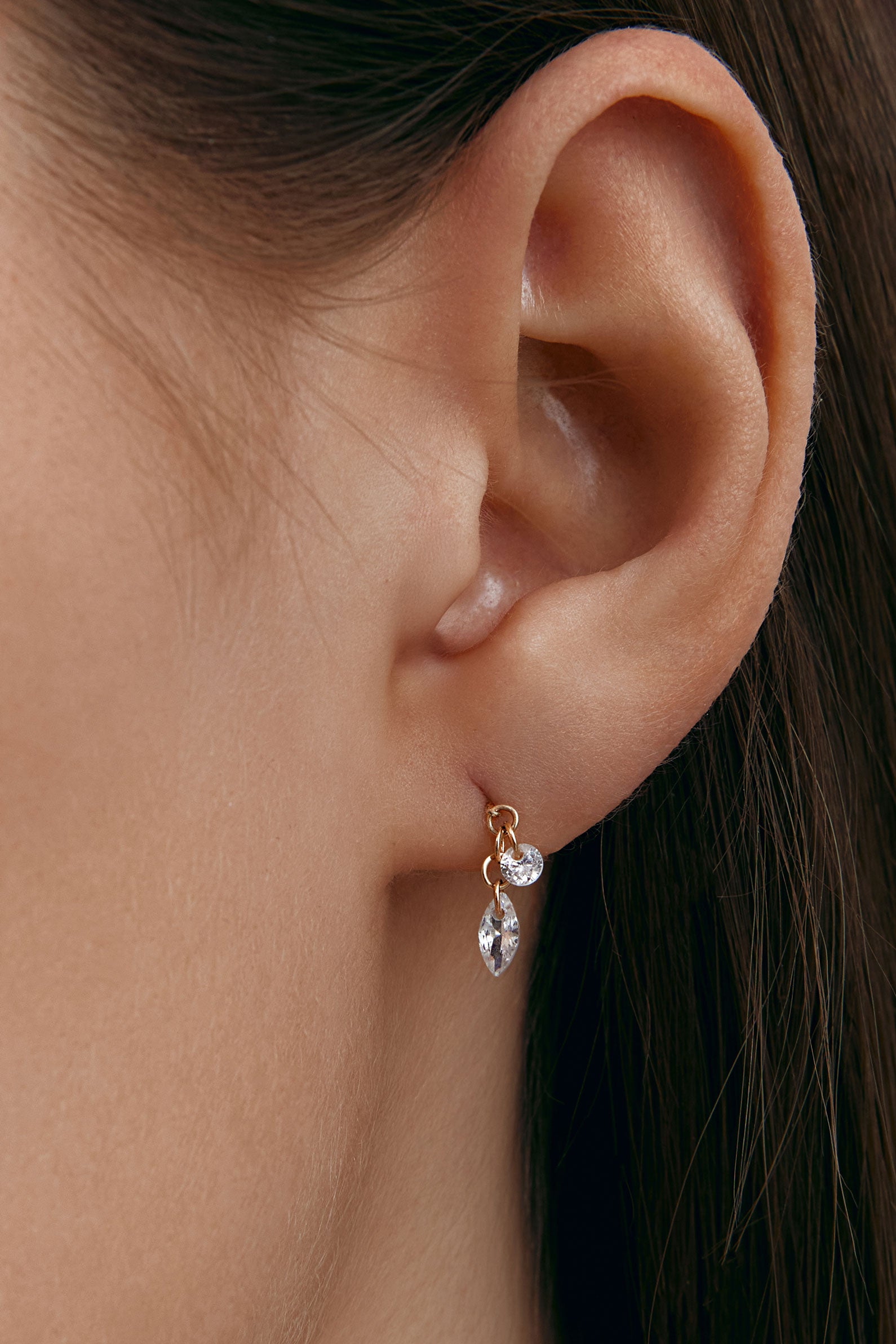Close-up of an ear wearing a delicate earring with a marquise cut gem