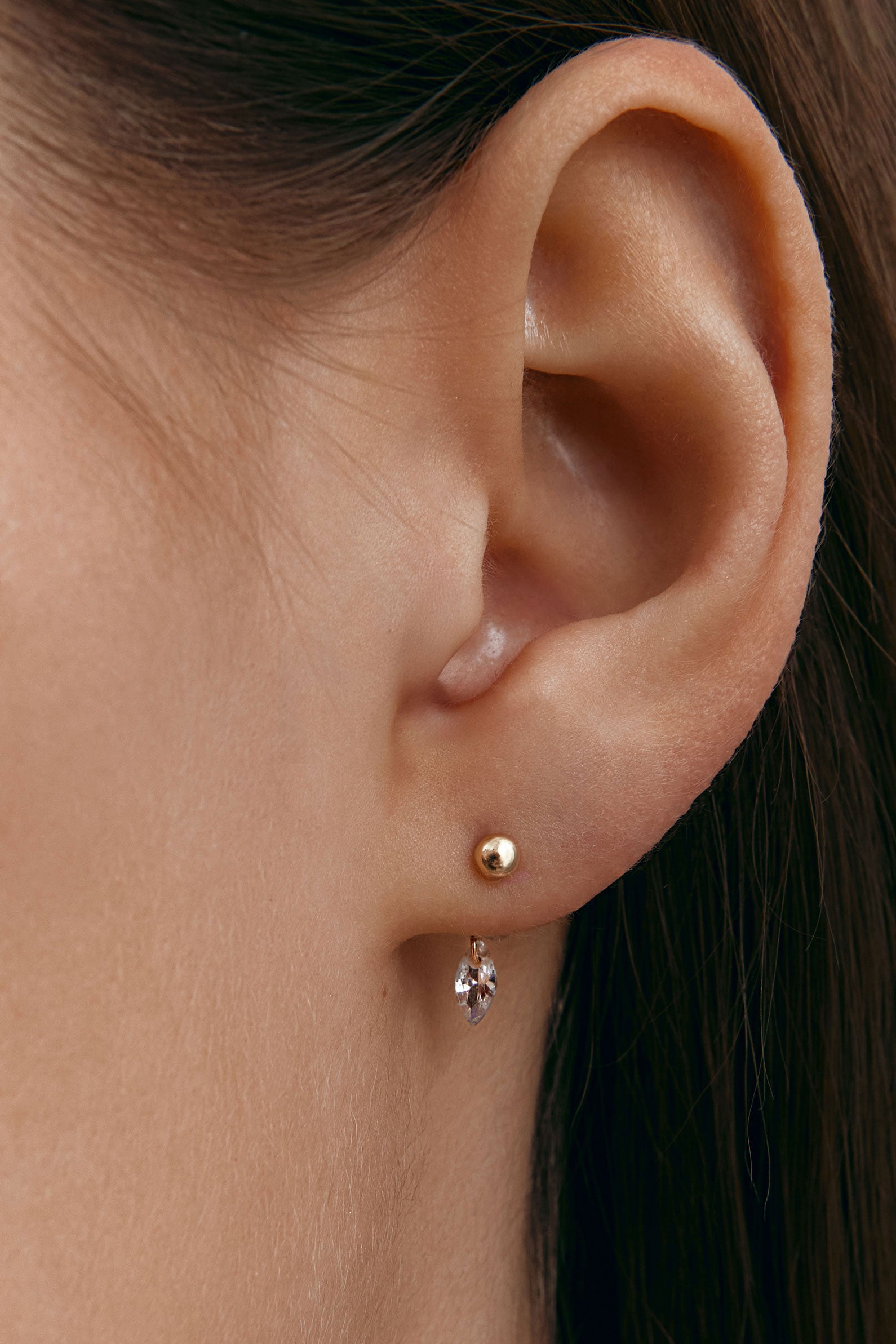 Close-up of an ear wearing a gold earring with a small marquise gemstone.