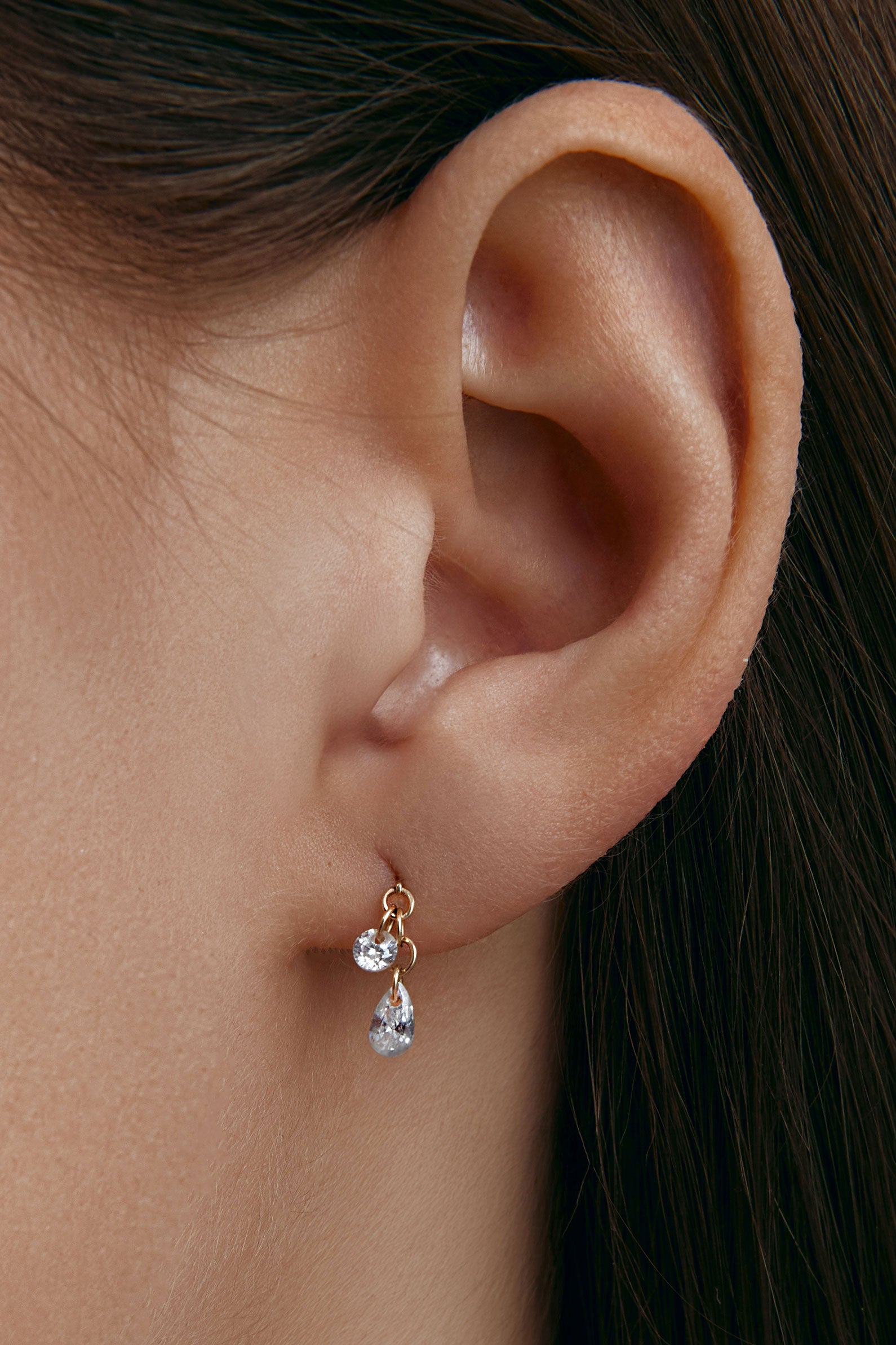 Ear wearing a gold earring with a pear-shaped gem 