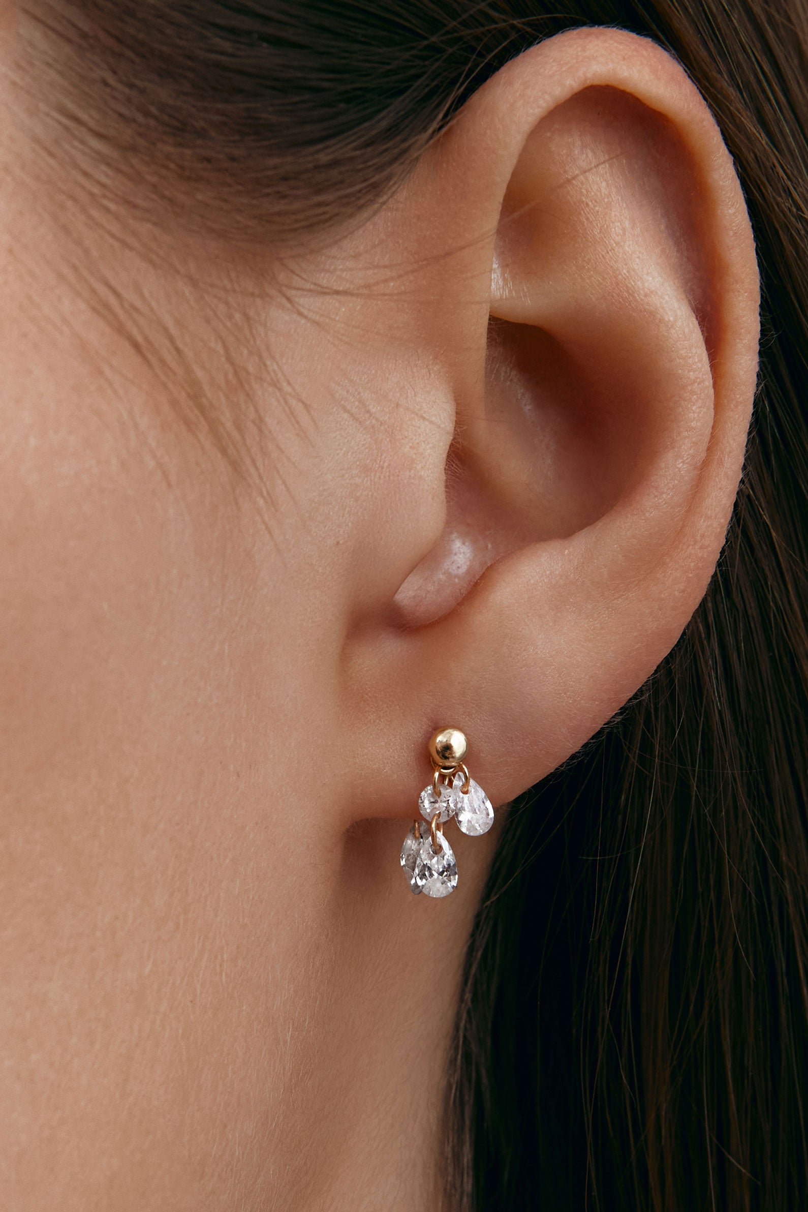 Close-up of an ear wearing a gold earring with pear-shaped gems