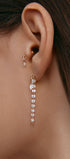 Close-up of an ear wearing a long gold earring with round gems