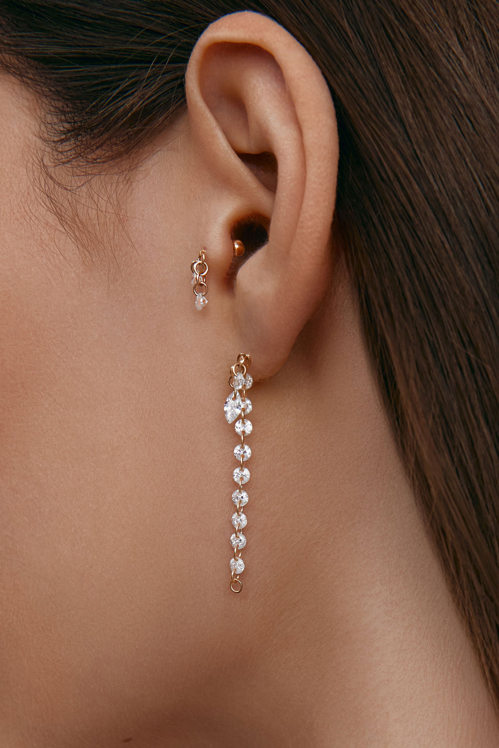 Close-up of an ear wearing a long gold earring with round gems