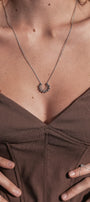Close-up of a necklace with a pendant on a person wearing a brown top.