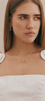 Woman wearing a silver necklace with a pendant against a neutral background