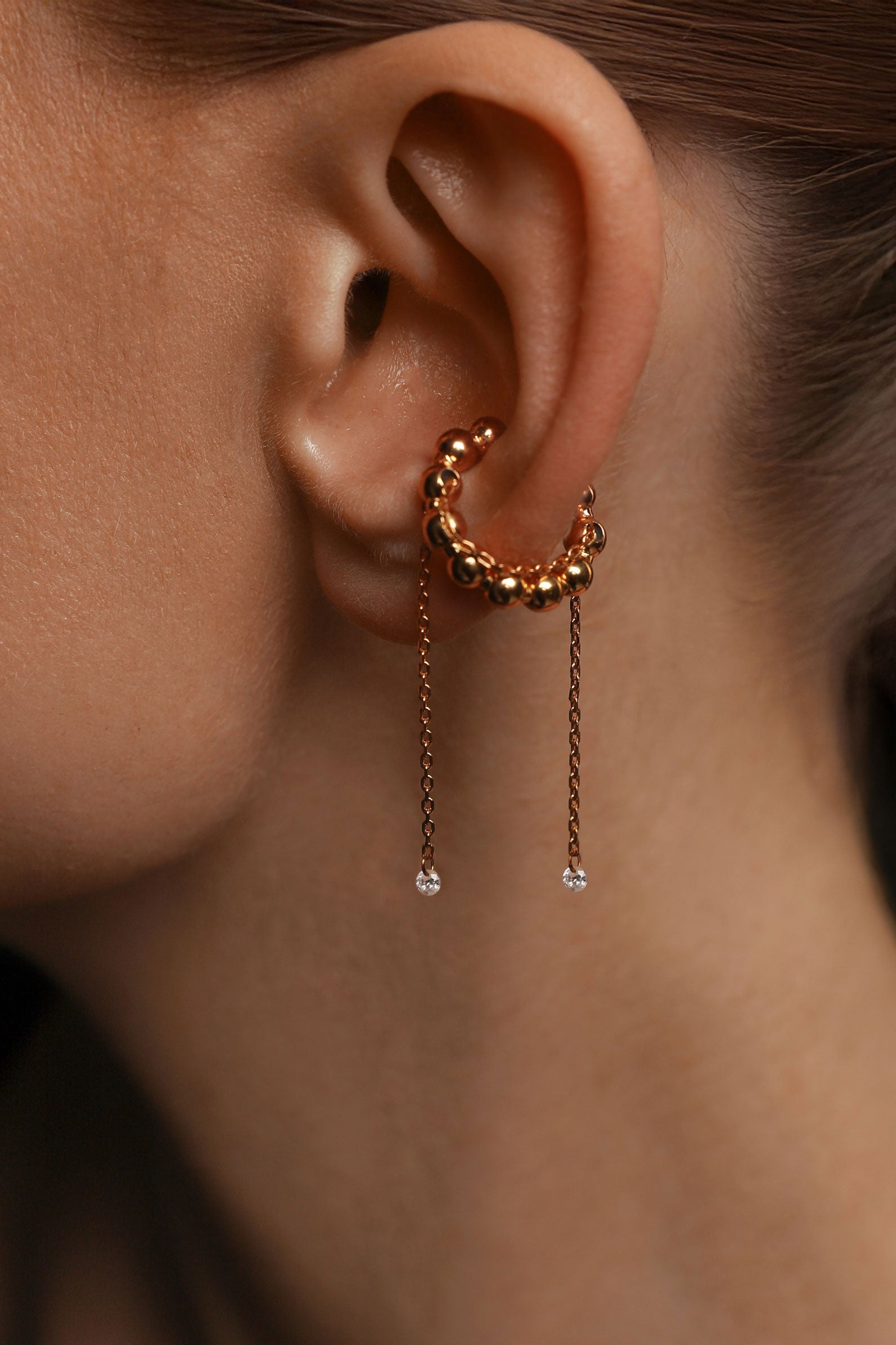 Close-up of an ear in a rose gold ear cuff with dangling gems